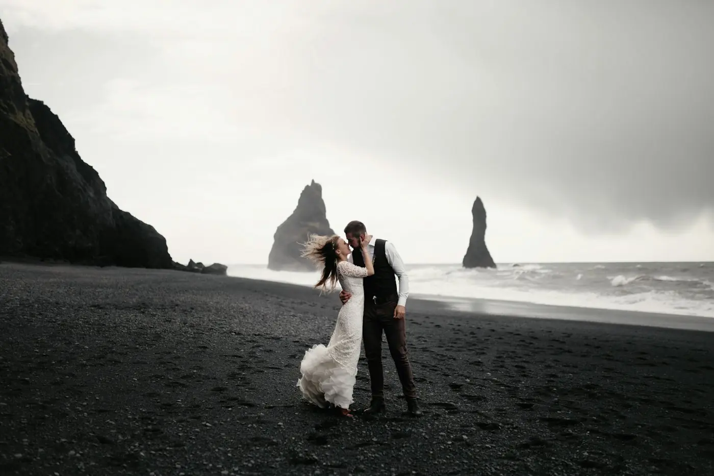 Bride and groom on a black sand beach under a dramatic sky