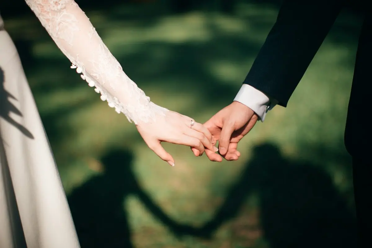 Bride and groom holding hands, their shadows on the grass