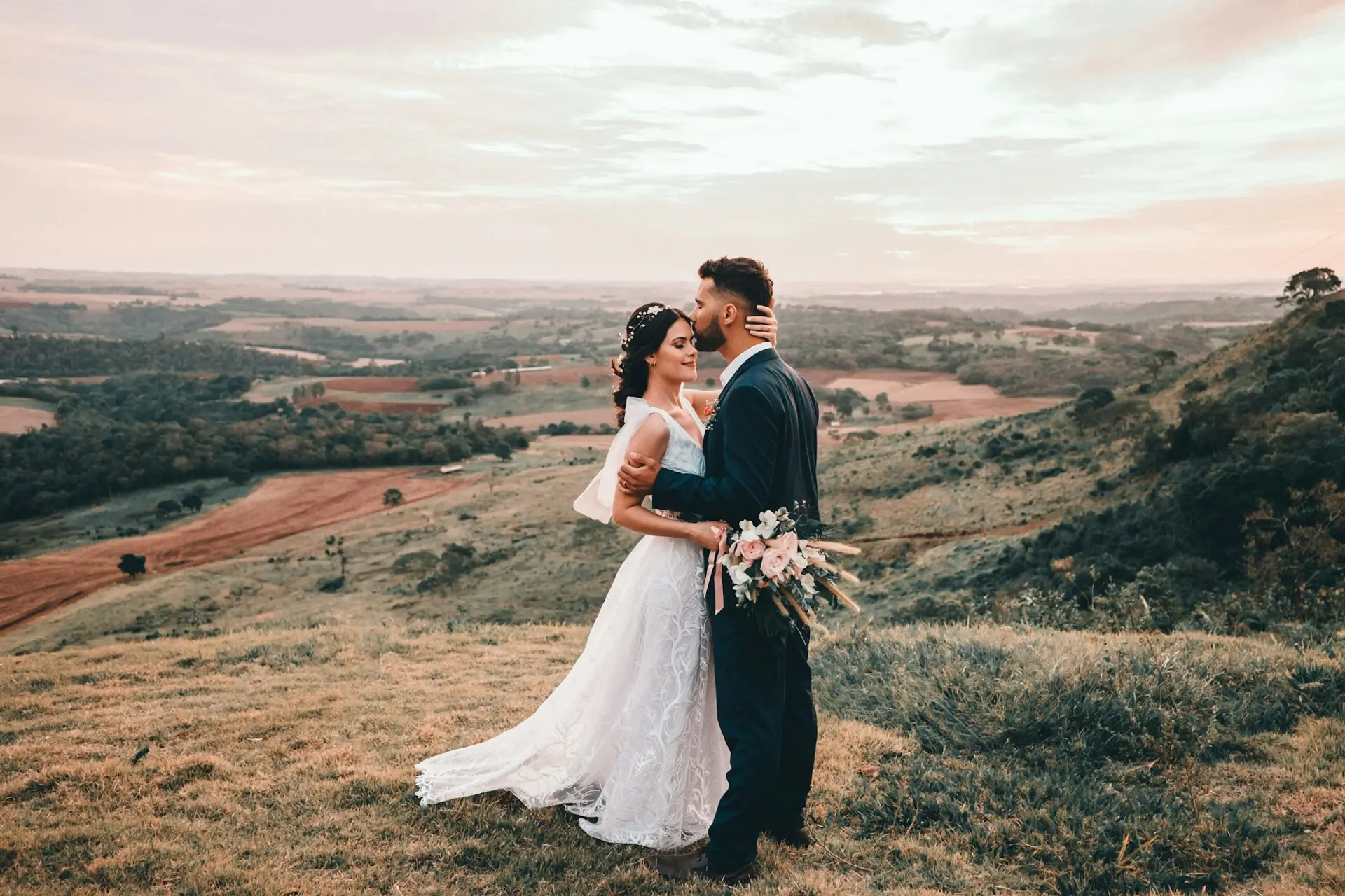 Couple embracing on a hillside above green countryside at sunset