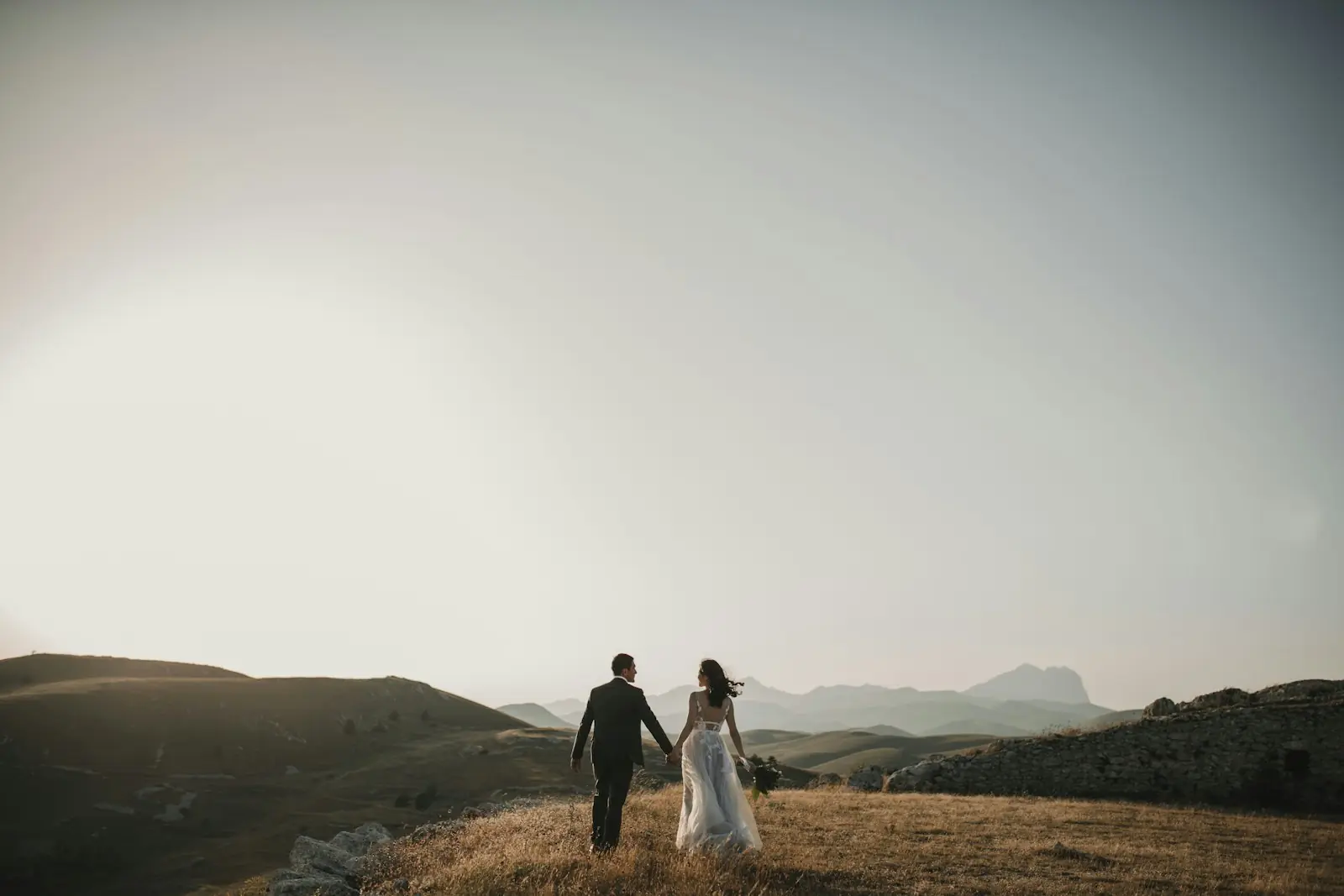 Couple walking hand in hand across a hilltop at dusk