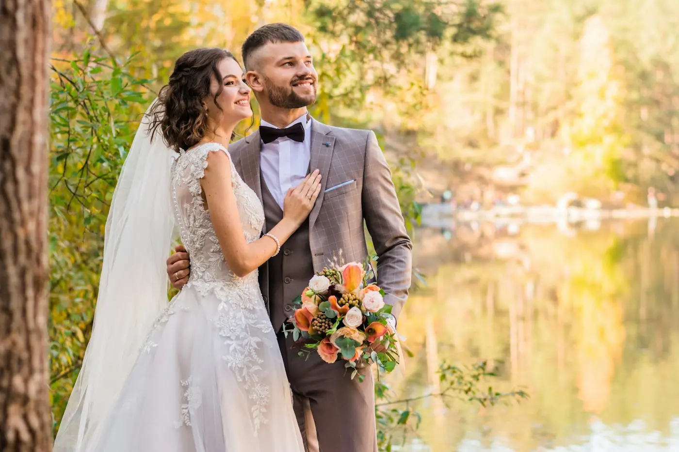 Bride and groom standing beside a lake in golden late-summer light
