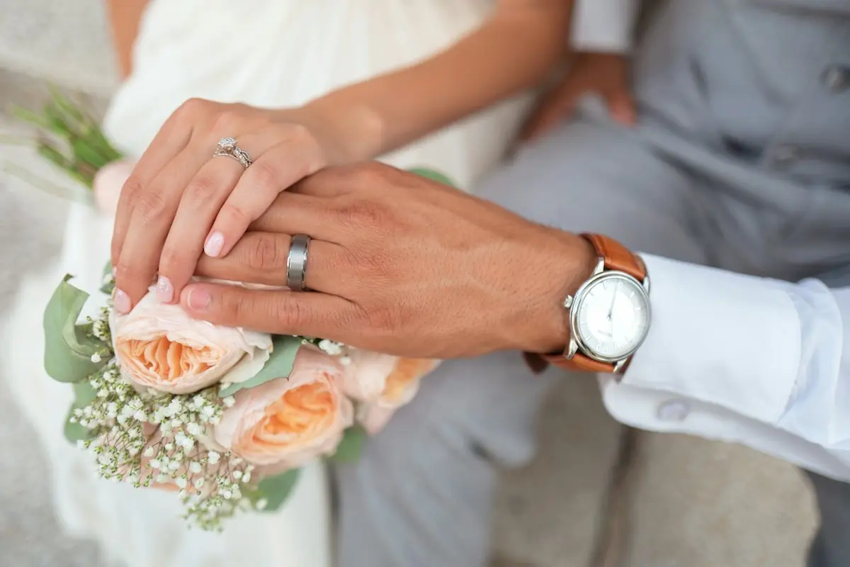 Close-up of wedding rings on the couple's joined hands over a bouquet